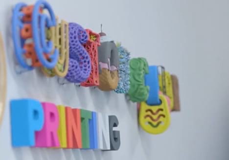 Colorful 3D printed letters spelling “Custom Printing” on a wall